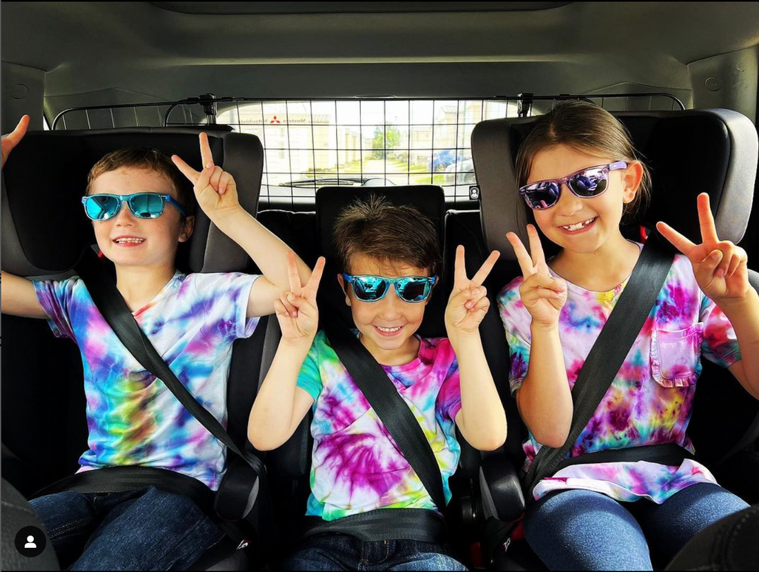 two boys and a girl wearing sunnies sunglasses in a car smiling.